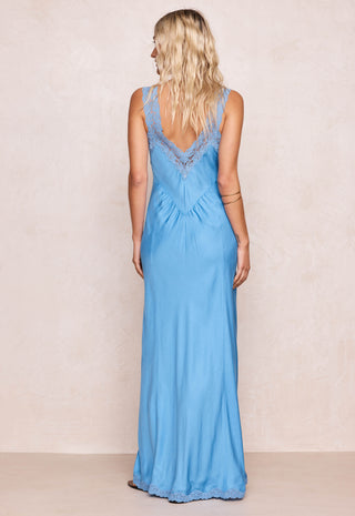 Back view of a woman wearing a blue maxi dress with lace panels against a beige background.