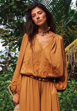 A woman wearing a bohemian-style mustard yellow embroidered top and matching pleated skirt