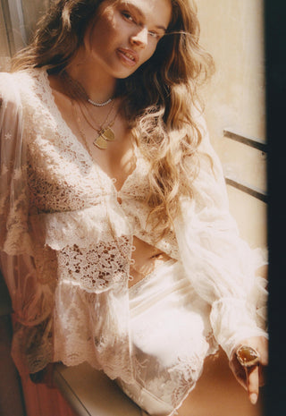 a-woman-wearing-a-white-lace-lingerie-set-with-a-sheer-long-sleeve-robe-styled-with-layered-gold-necklaces-in-warm-sunlit-indoor-lighting