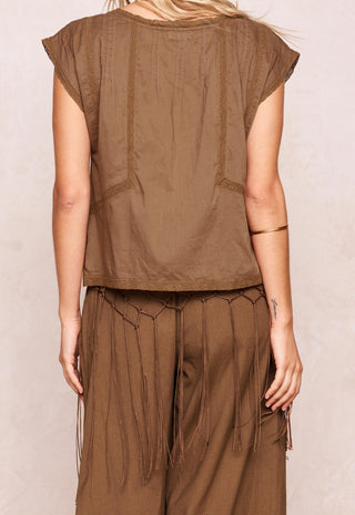 A woman shown from the back wearing a brown sleeveless top and matching brown fringe pants against a light beige textured wall.