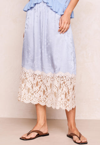 A light blue midi skirt with a cream lace hem, shown on a model wearing brown thong sandals against a neutral beige background.
