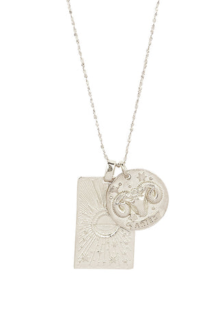 Close up front view of Spell’s Aries Stargazer Zodiac Necklace charms. One charm is of a rectangular shape and features a sun with stars while the other charm is circular and features the Zodiac label and icon.