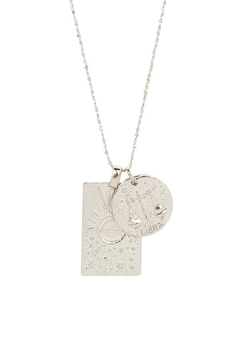 Close up front view of Spell’s Libra Stargazer Zodiac Necklace charms. One charm is of a rectangular shape and features a sun with stars while the other charm is circular and features the Zodiac label and icon.